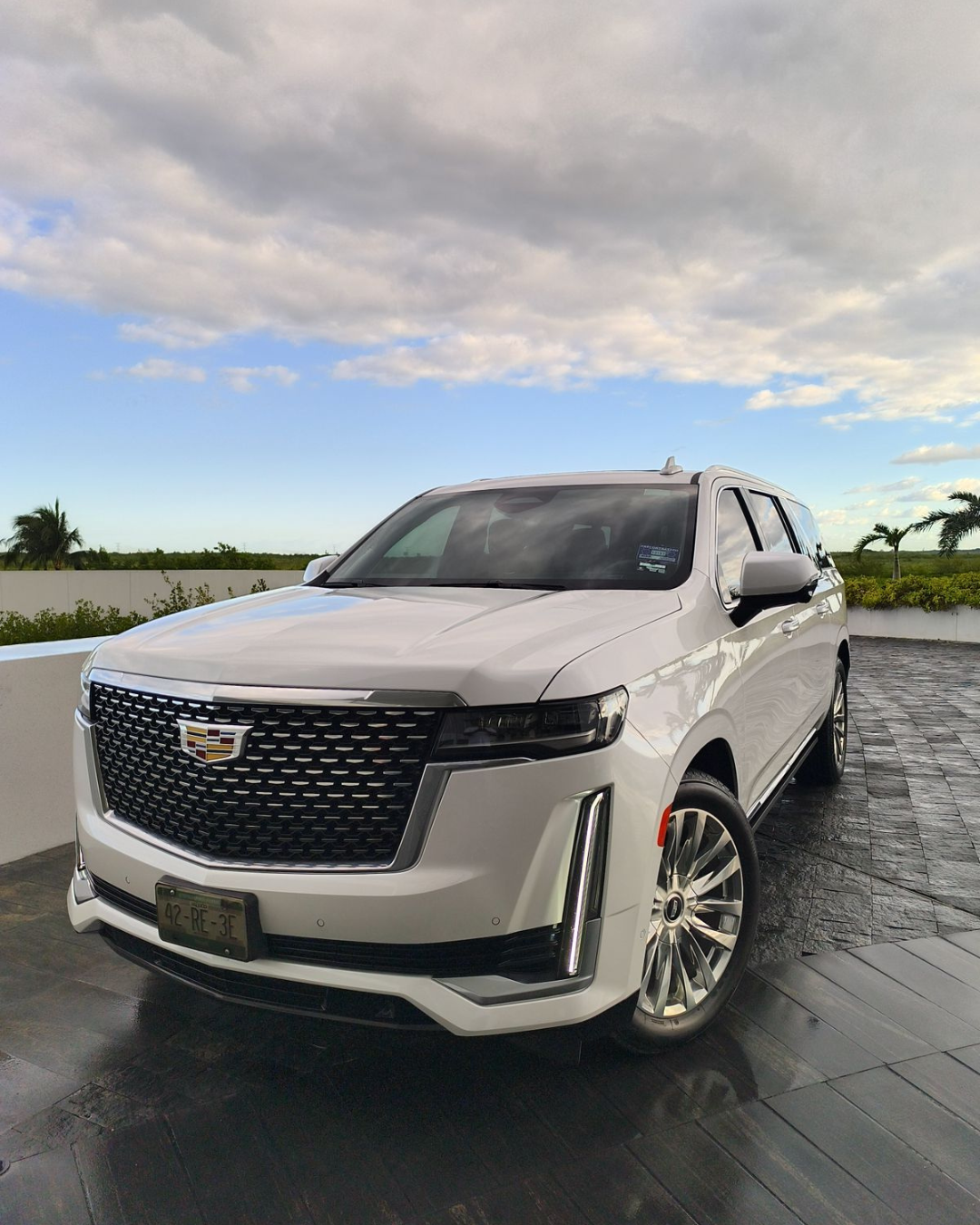 A white Cadillac SUV is parked on a driveway under a partly cloudy sky, special for cancun luxury transportation