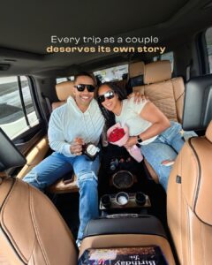 A smiling couple sits in the backseat of a luxury car, holding a bouquet of roses and a bottle, highlighting that every trip as a couple deserves its own story—make yours unforgettable with Cancun wedding transportation. 