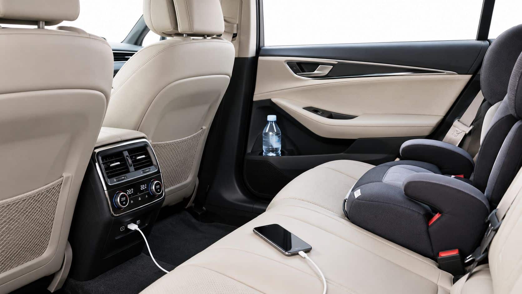 A luxurious car backseat with a child car seat, a smartphone charging, and a water bottle.